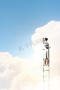 爬梯子的人摄影照片_站在梯子上的女商人在多云的背景下眺望远方