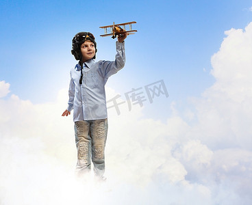 戴着飞行员头盔的小男孩在云的背景下玩玩具飞机