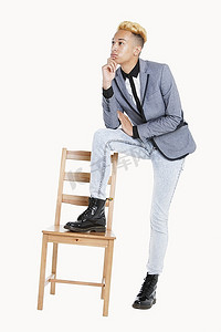 深思熟虑的十几岁男孩站在灰色背景上，一条腿放在椅子上