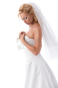 美丽的新娘，金发，摆出性感的姿势，穿着优雅的礼服，戴着面纱，手上有花卉装饰。