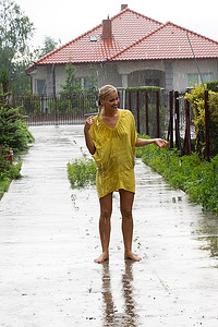 穿着黄色连衣裙的年轻金发女子在雨中飘落在屋外