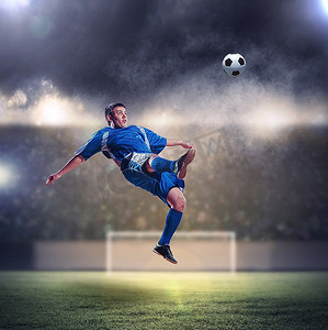 蓝色衬衫摄影照片_身着蓝色衬衫的足球运动员在体育场高空击球