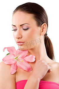 在白色背景下，肩上戴着一朵粉色的百合花，美丽女子脸上的皮肤清新、透明、健康