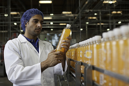 装瓶摄影照片_灌装厂工人在检查橙汁瓶
