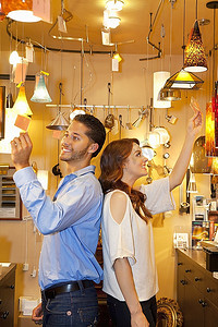 幸福的年轻夫妇背靠背地站在灯具店里看价签