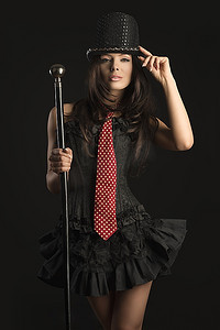 性感的卡巴莱女演员，穿着黑色紧身胸衣，打着红色领带，戴着帽子，留着棕色的头发，手拿棍子摆出性感的姿势