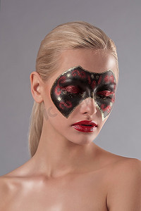 一位涂着红色口红、脸上画着狂欢节面具的金发美女的面部照片