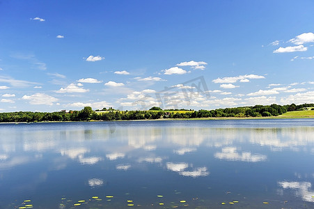 平静的湖水，对岸的树林和蔚蓝的天空。景观