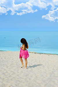 一个孤独的女孩，穿着一件红色的斗篷走在海边的海滩上