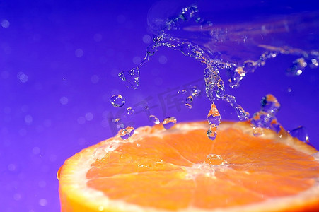 果汁液体飞溅摄影照片_明亮多汁的橙色，在紫色的背景上飞溅