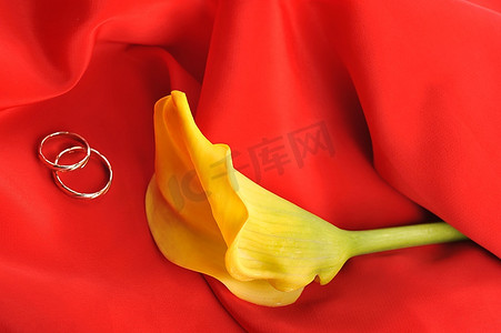红色优雅的面料、黄色的鲜花和结婚戒指近在咫尺