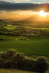 云层太阳摄影照片_乡村、丘陵和山谷的美丽风景，夕阳照亮山坡，阳光穿透戏剧性的云层