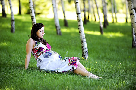美丽的女人坐在桦树林的草地上。夏天的一天