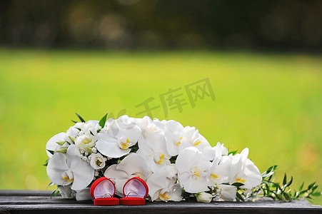 花束的白色兰花和婚礼金戒指在木长凳上