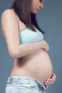 孕期摄影照片_身着蓝色衬衫的美丽孕妇白人。一头黑色的长发。手放在肚子上。孕期收藏。