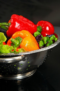 蔬菜落摄影照片_新鲜洗净的新鲜蔬菜在隔绝在黑色背景上的金属滤器中。