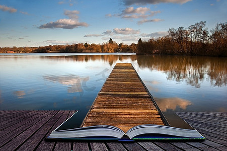 美丽的日落风景，平静的湖面上的木制钓鱼码头，在魔法书中的页面上映出清晰的倒影