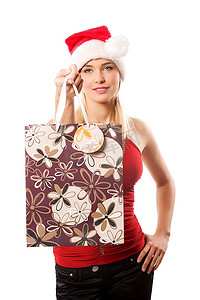 年轻的金发女子穿着红色上衣，戴着圣诞帽，拿着购物袋，戴着卡马拉微笑着
