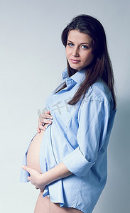 身着蓝色衬衫的美丽孕妇白人。一头黑色的长发。手放在肚子上。孕期收藏。