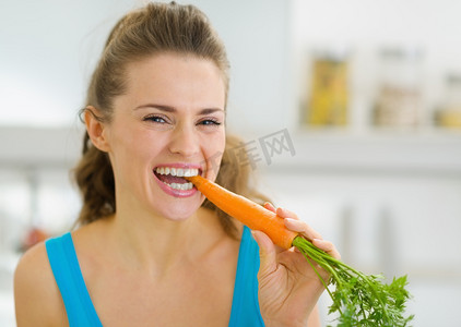 快乐的年轻女人在厨房里吃胡萝卜