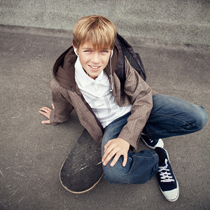 小学生裤子摄影照片_学校青年坐在学校附近的滑板上