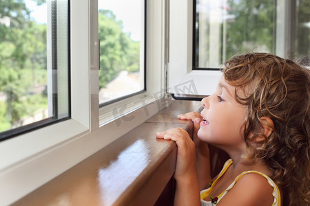 夏天美酒摄影照片_漂亮微笑着阳台上的小女孩，从窗口看