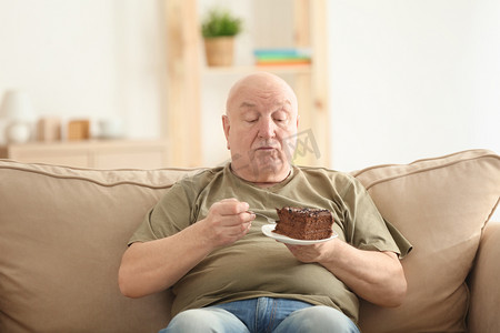 高级胖子吃蛋糕时坐在家里的沙发上。重量损失概念
