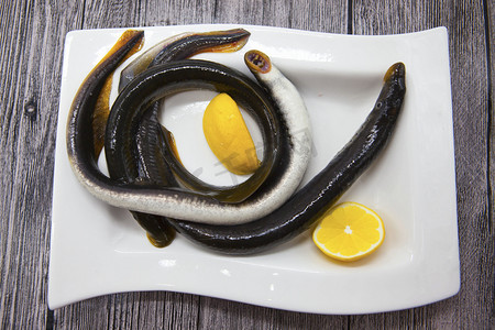 plate摄影照片_Fresh live fish lamprey on porcelain plate with lemon.
