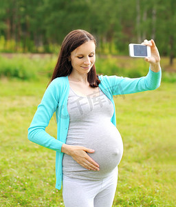 Happy young pregnant woman makes self-portrait on the smartphone