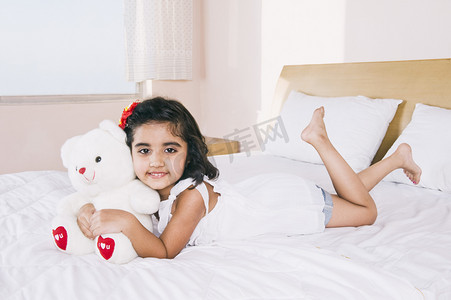 一个女孩躺在床上抱着一只泰迪熊和微笑的画像