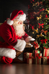 新年海报线下摄影照片_在黑暗的房间里放在圣诞树下的礼物的圣诞老人