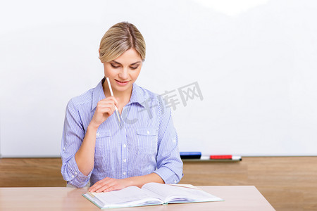 被教训摄影照片_Teacher at the desk checking her register.