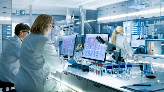 女性和男性科学家们致力于大现代实验室在他们的计算机。各种货架与烧杯、 化学品和不同的技术设备是可见.