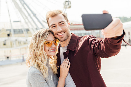 建筑手机摄影照片_微笑的情侣在秋季服装采取自拍智能手机在城市