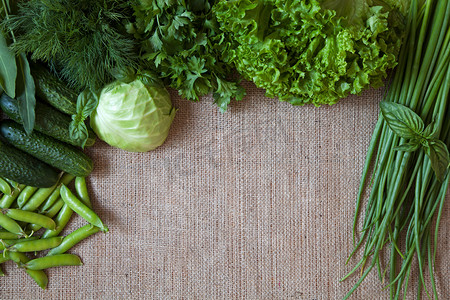 辣白菜面摄影照片_绿色蔬菜构图质朴麻布背景上。豌豆、 白菜、 黄瓜、 罗勒、 莳萝、 洋葱,