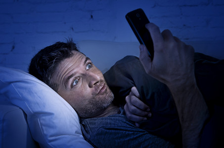 man in bed couch at home late at night using mobile phone in low