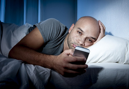 不能成为理由摄影照片_年轻的手机瘾君子男人在床上使用智能手机的夜不能眠