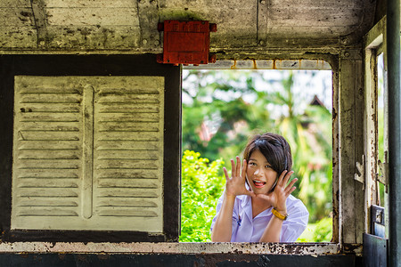 玩呢摄影照片_可爱的亚洲泰国女学生穿制服给一个惊喜呢通过旧复古窗口面板。没有人会将吓倒?