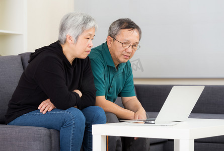 年长的夫妇与便携式计算机在家里工作 