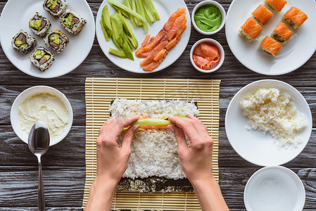 裁切拍摄的人烹饪美味的寿司卷与鲑鱼, 鳄梨和黄瓜