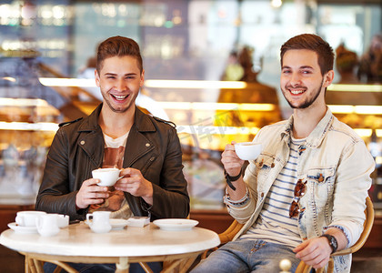 两个年轻时髦的家伙坐在咖啡厅聊天，喝咖啡微笑