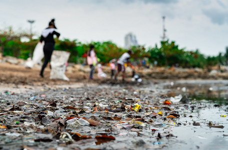 u志愿者摄影照片_收集垃圾的志愿者的模糊。海滩环境污染。志愿者打扫海滩。整理海滩上的垃圾。海滩上有油渍。石油泄漏到海洋.