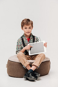 使用電腦摄影照片_逗人喜爱的小男孩显示数字式片剂与空白的屏幕和看照相机隔绝在灰色