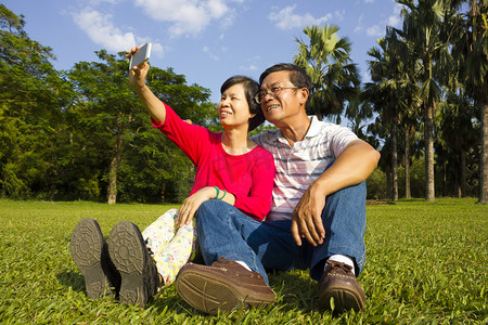 亚洲高级夫妇坐在草地和拍照 