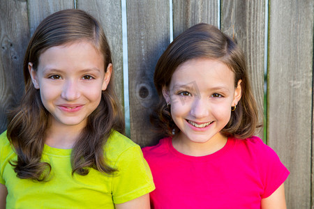 姊妹峰摄影照片_快乐双胞胎姐妹在木后院篱笆上微笑