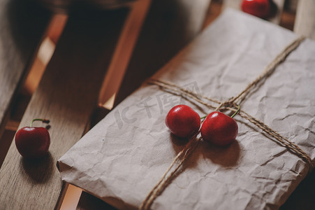 fresh cherries on plate with wrapped gift on wooden table. Vintage toned, farm life concept. Selective focus. Home growth summer berries