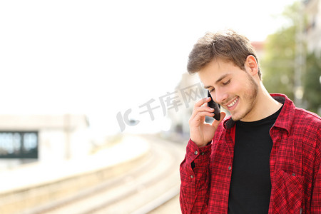 火车剪影摄影照片_Teen guy calling on the mobile phone waiting a train