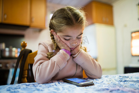 科技小子摄影照片_小金发女孩扎着辫子看一部智能手机