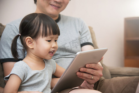 亚洲孩子和她父亲坐和使用数字平板电脑一起