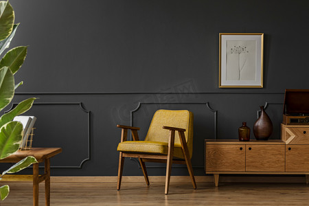 复古设计海报摄影照片_宽敞的, 老式的起居室内有黑色的墙壁, 木地板, 黄色的椅子, 海报和植物